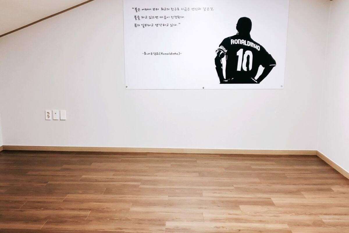 A room with a wooden floor and a wall-mounted poster of a soccer player.
