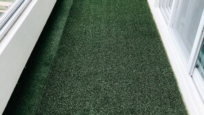 A narrow, green artificial grass pathway between two white walls with windows. - Leeds Pension (Seogwipo)