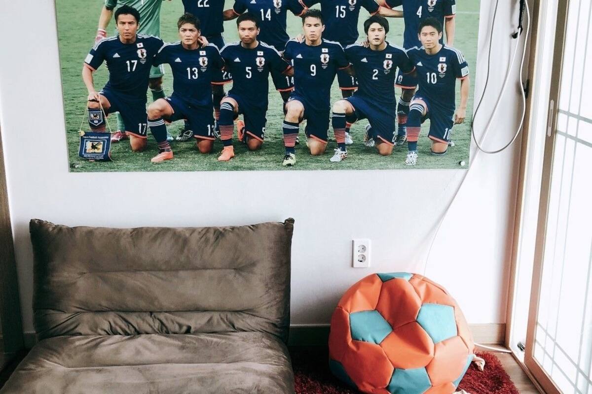 A bedroom with a bed, a wall-mounted poster of a soccer team, and a window with a view.