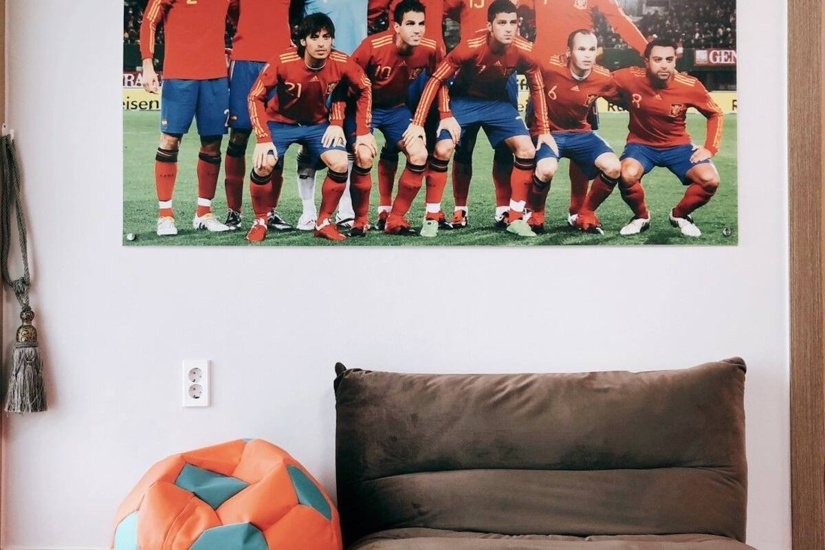 A room with a brown sofa, a colorful bean bag, and a sports team photo on the wall.