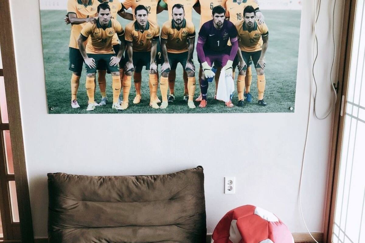 A room with a brown sofa, a soccer ball, and a poster of a soccer team on the wall.
