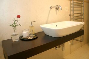 Un baño con un lavamanos blanco tipo pedestal, un perchero y un frasco de vidrio con una rosa roja.