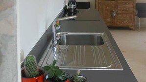 Une cuisine avec un évier en acier inoxydable, un meuble en bois et trois plantes en pot rouges posées sur le plan de travail.