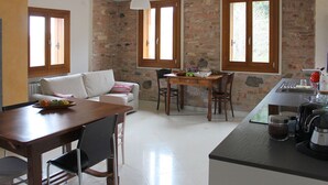 Une cuisine avec une table à manger, des chaises, une machine à café et un mur en pierre.