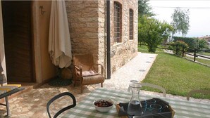 Une terrasse extérieure avec une nappe à carreaux, des chaises en osier, un bâtiment en pierre et une vue sur la verdure environnante.