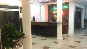 A hotel reception area with a reception desk, a neon sign, and a potted plant.