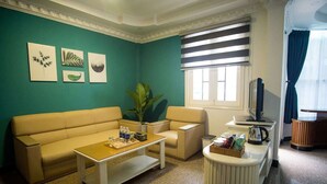 A living room with a beige sofa, a coffee table, a TV, and a window with blinds.
