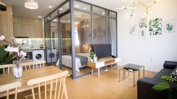 A modern living space with a dining area, a sofa, a TV, and a kitchen area visible through a glass partition.