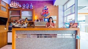 A hotel reception desk with a wooden counter, a large anchor logo, and various decorative items including model ships and figurines. - Phusamor Hotel (Trang)
