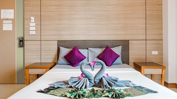 A hotel room with a large bed, two nightstands, a wooden headboard, and a decorative swan arrangement on the bed. - Phusamor Hotel (Trang)