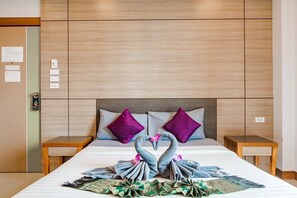 A hotel room with a large bed, two nightstands, a wooden headboard, and a decorative swan arrangement on the bed.