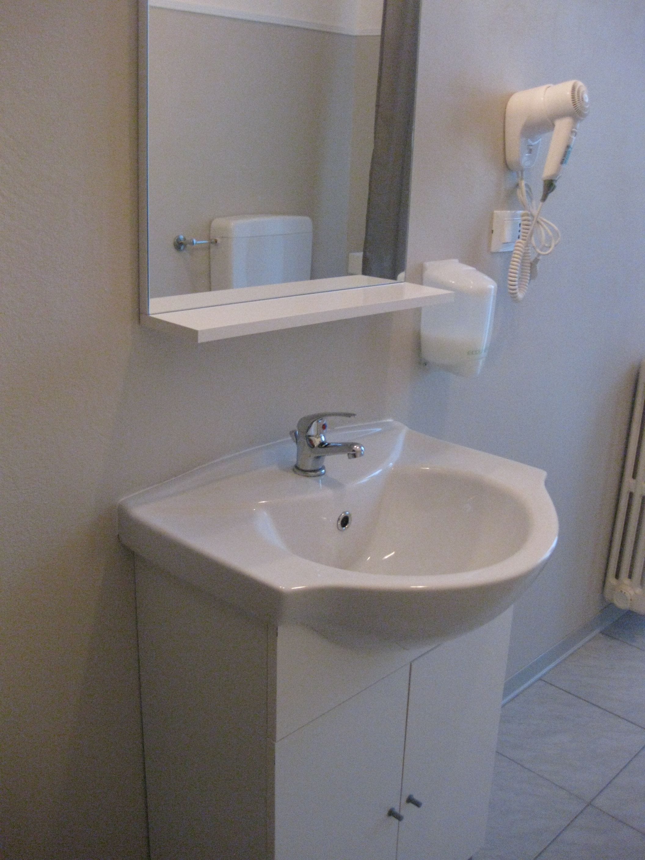 A bathroom with a white sink, a mirror, a hairdryer, and a toilet.