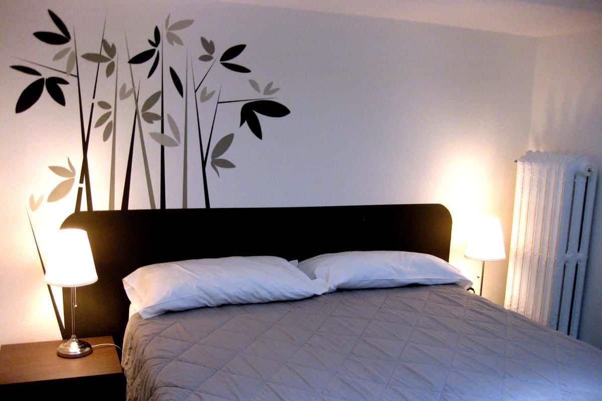 A neatly made bed with a quilted cover, two bedside lamps, and a wall decoration of stylized leaves.