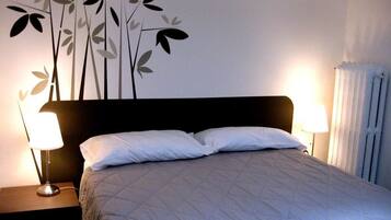A neatly made bed with a quilted cover, two bedside lamps, and a wall decoration of stylized leaves.
