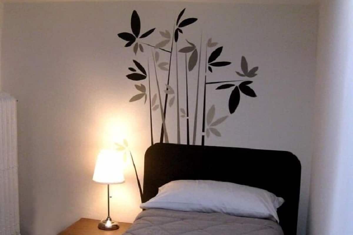 A single bed with a white duvet in a room with a wall-mounted decorative panel featuring leaves and branches.