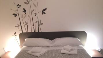 Una cama bien tendida con sábanas y toallas blancas, un cabecero oscuro y una decoración de hojas estilizadas.