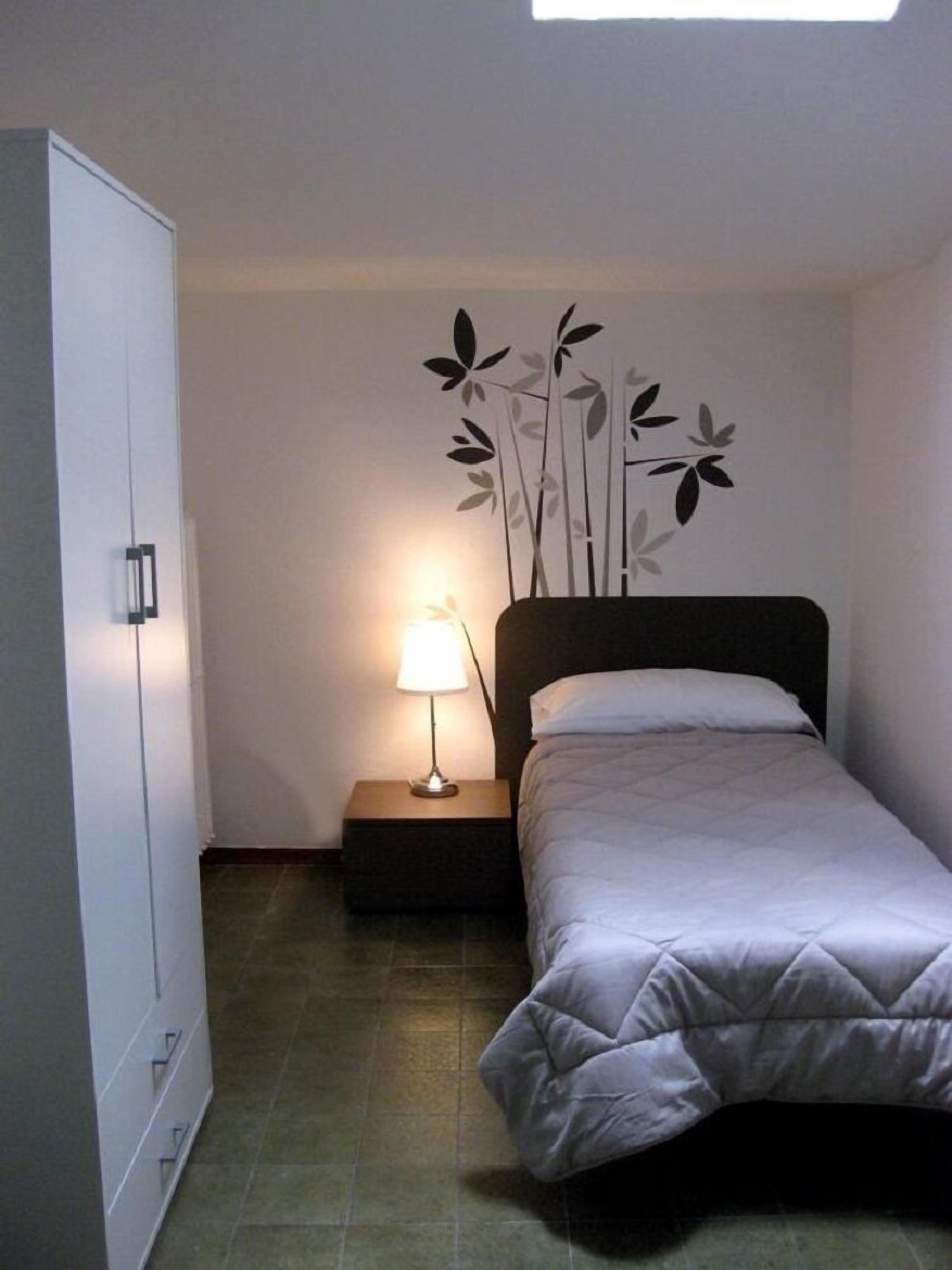 A bedroom with a bed, a nightstand, a lamp, a wardrobe, and a wall decoration.