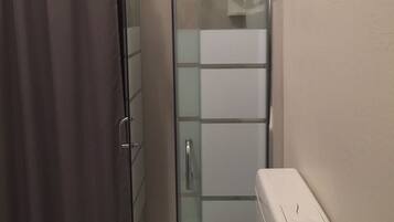 Un baño con cabina de ducha de vidrio, inodoro y una toalla colgada en la puerta de la ducha.