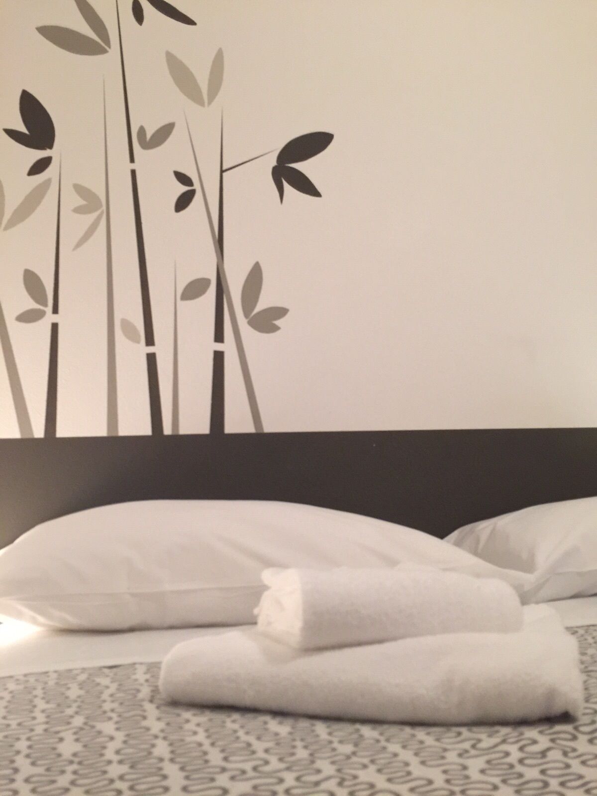 Ein Bett mit weißen Kissen und gefalteten Handtüchern, ein gemustertes Teppich und eine Wand mit einem Bambus-Pflanzenmuster.