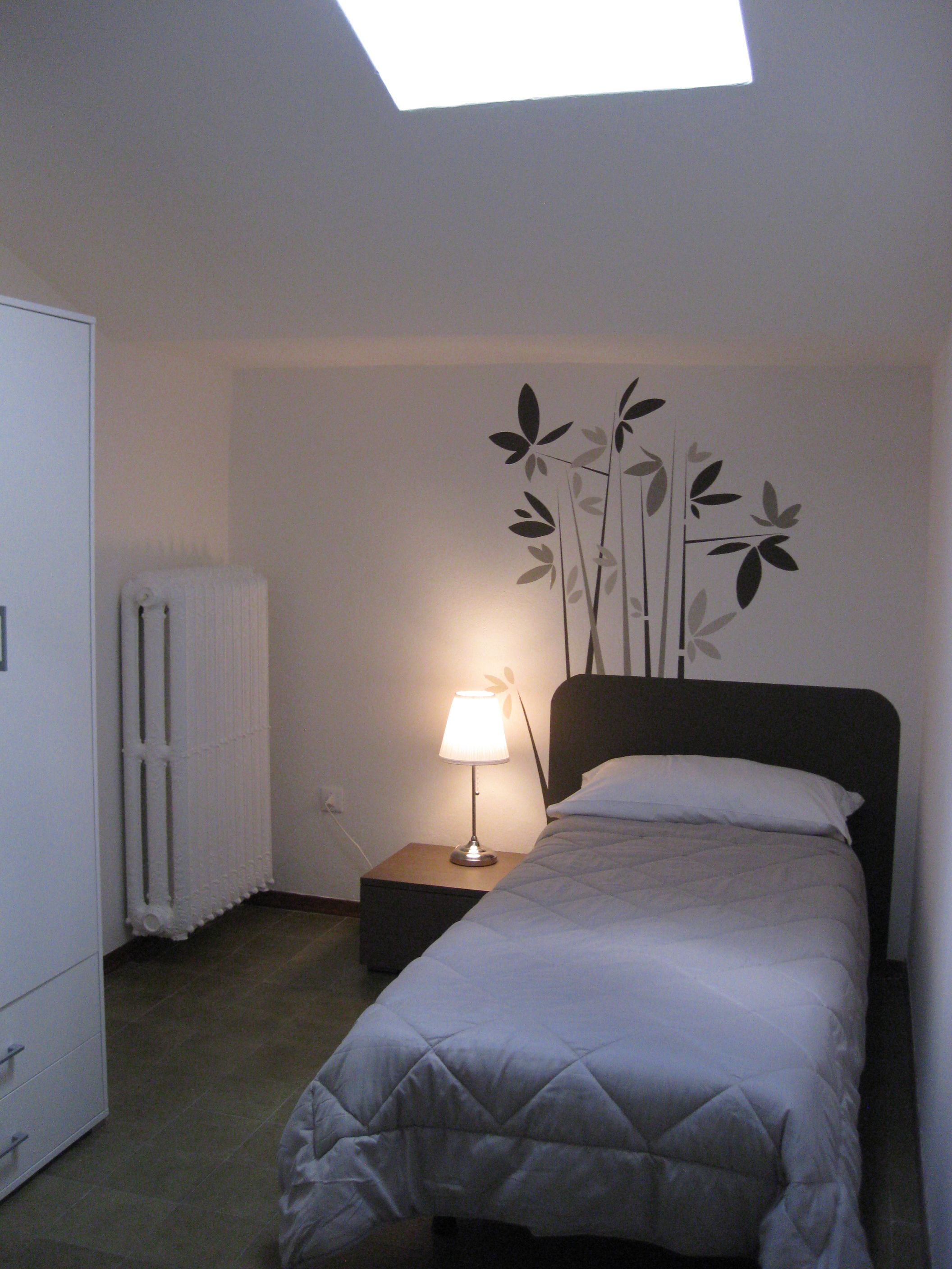Un dormitorio con una cama, una mesita de noche con lámpara, un radiador y una pared decorada con diseño floral.