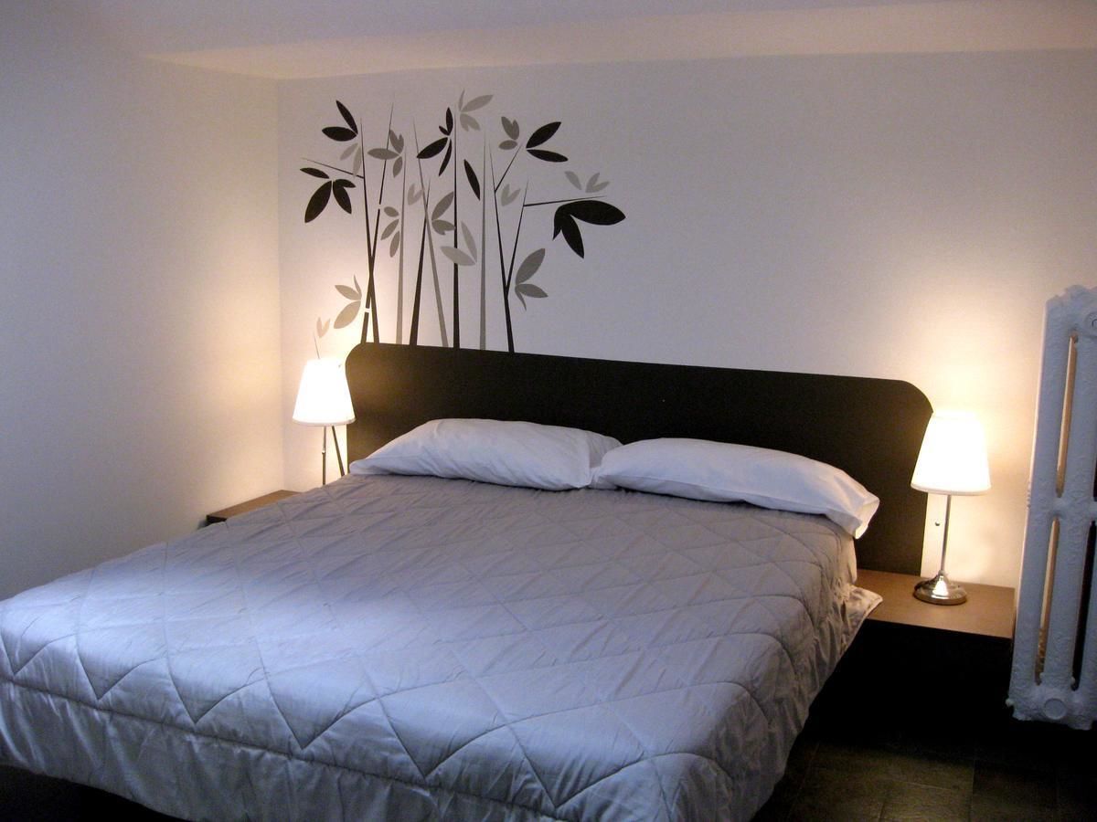 A neatly made bed with a quilted cover, two bedside lamps, and a wall decoration of stylized plants.