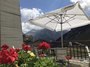 A terrace with outdoor seating, a large umbrella, and a mountain view. - Hotel Edelweiss Candanchu (Aisa)