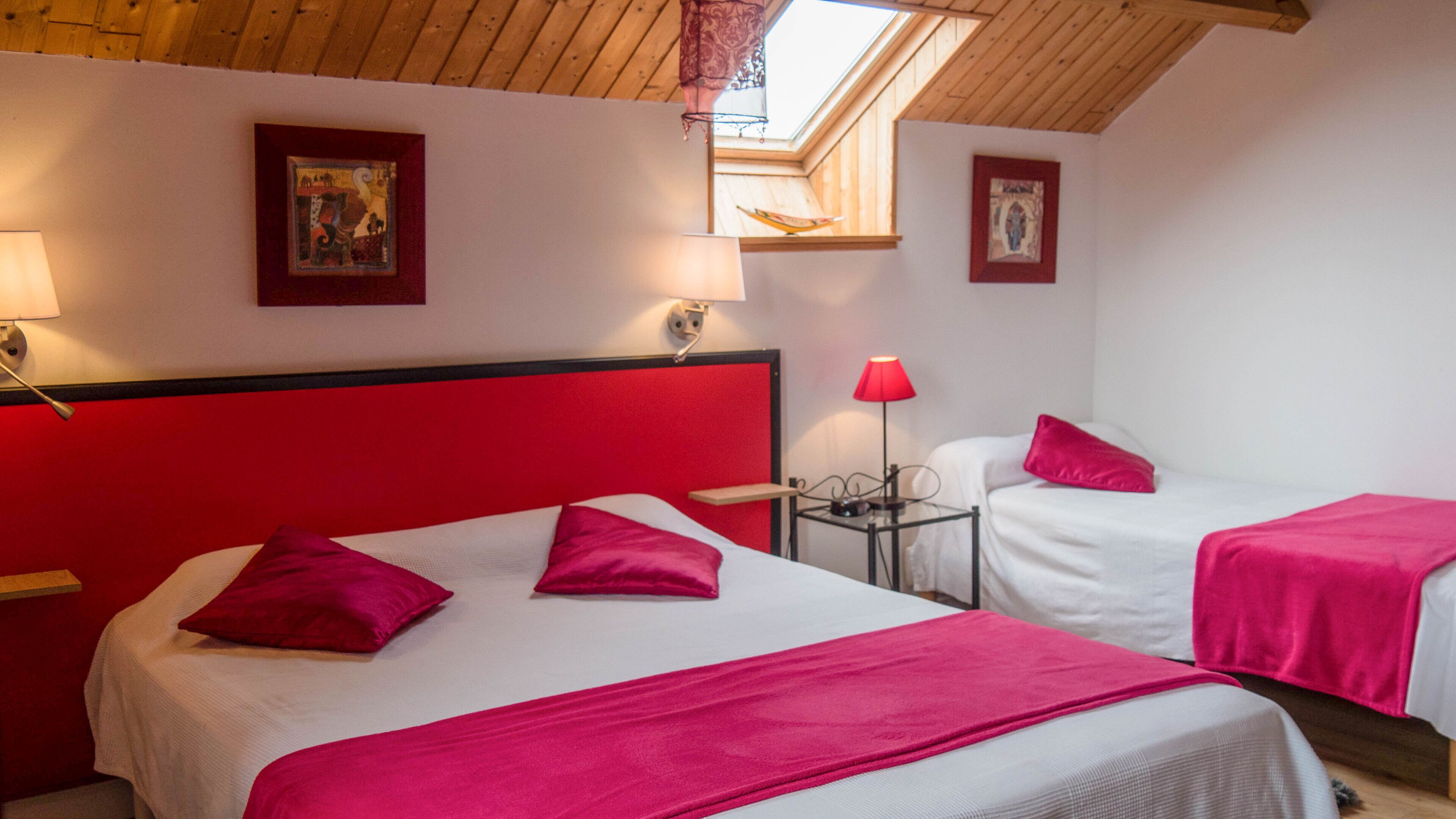 A hotel room with two beds, red headboards, and white bedding. There are two wall-mounted lamps and a skylight above the beds.