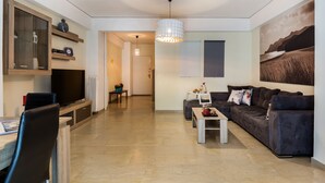 Ein modernes Wohnzimmer mit Flachbildfernseher, einer dunkelgrauen Couch, einem Couchtisch und einer Pendelleuchte.