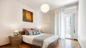 Ein Schlafzimmer mit Holzboden, einem Bett mit gemustertem Überwurf, einem Nachttisch mit Lampe, einem Bild an der Wand und einem Fenster mit Vorhängen.