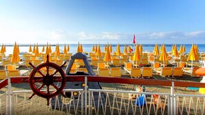 Una playa con hileras de sillas amarillas y sombrillas naranjas, un volante y una barandilla.