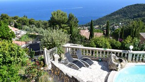 A pool area with lounge chairs, a stone deck, and a view of the sea and hills. - VILLA SOLARIS Independent studio in villa with pool (Alpes-Maritimes)