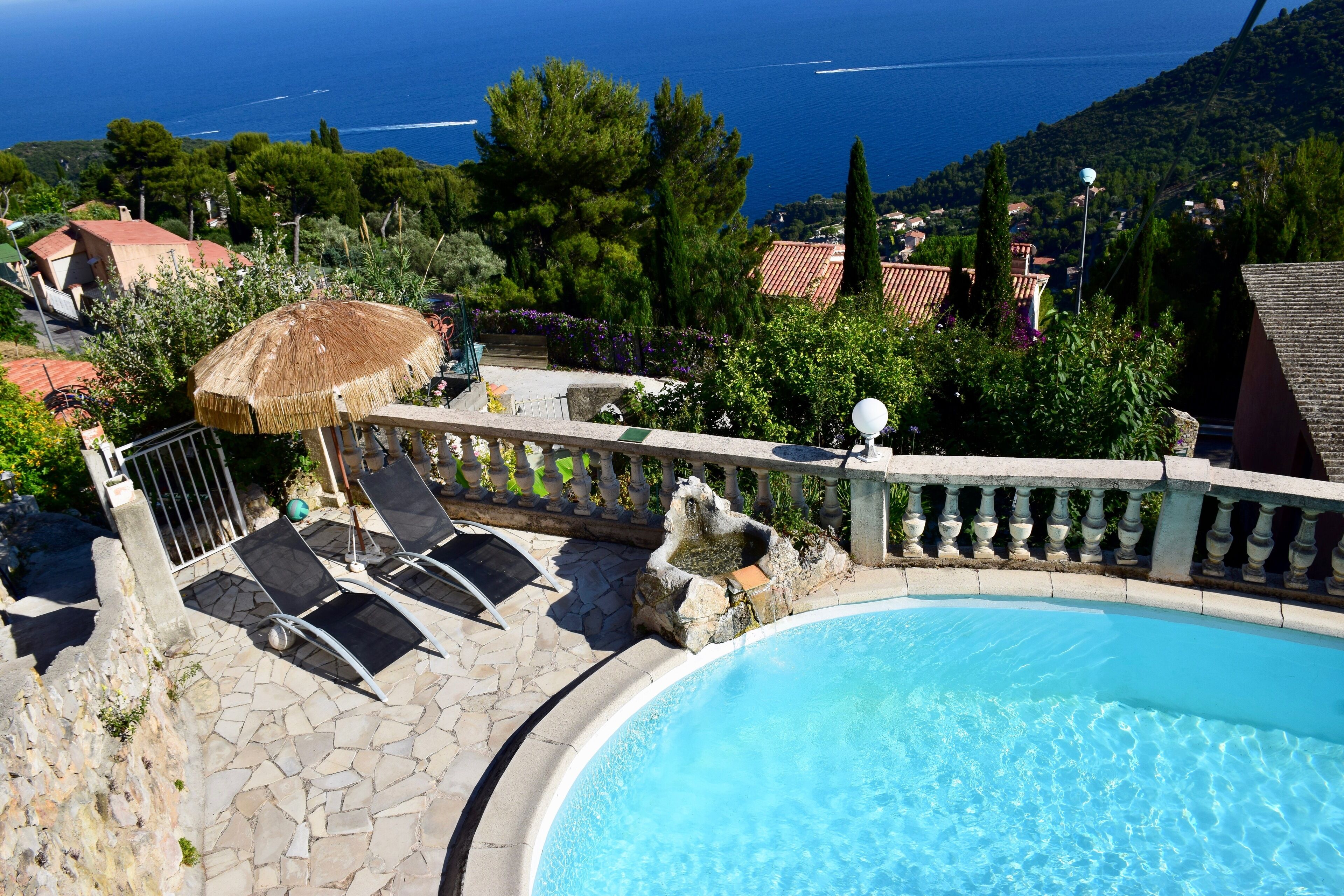 A swimming pool with a stone deck, lounge chairs, and a thatched umbrella.