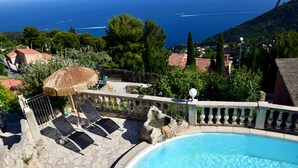 A swimming pool with a stone deck, lounge chairs, and a thatched umbrella. - VILLA SOLARIS Independent studio in villa with pool (Alpes-Maritimes)