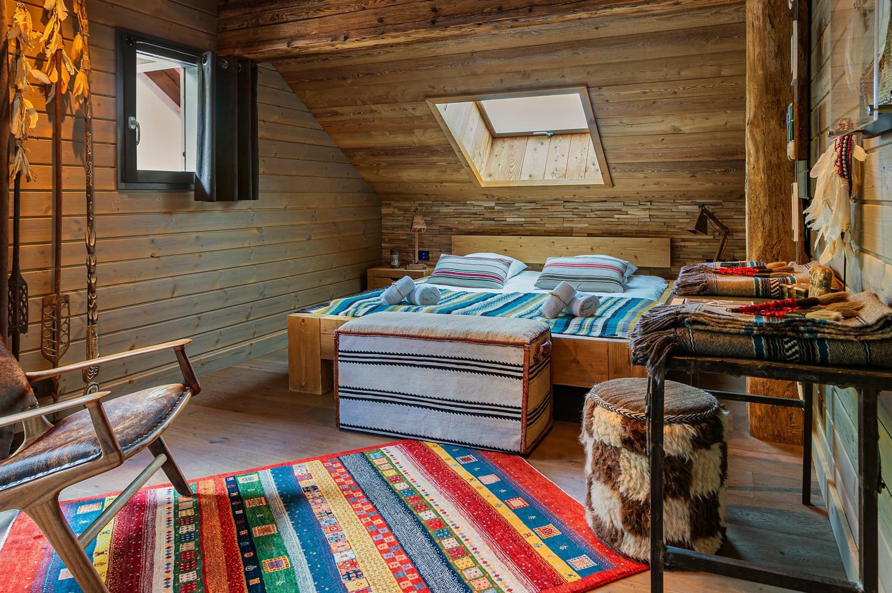 A cozy log cabin bedroom with a loft bed, a colorful rug, and a small table with blankets.