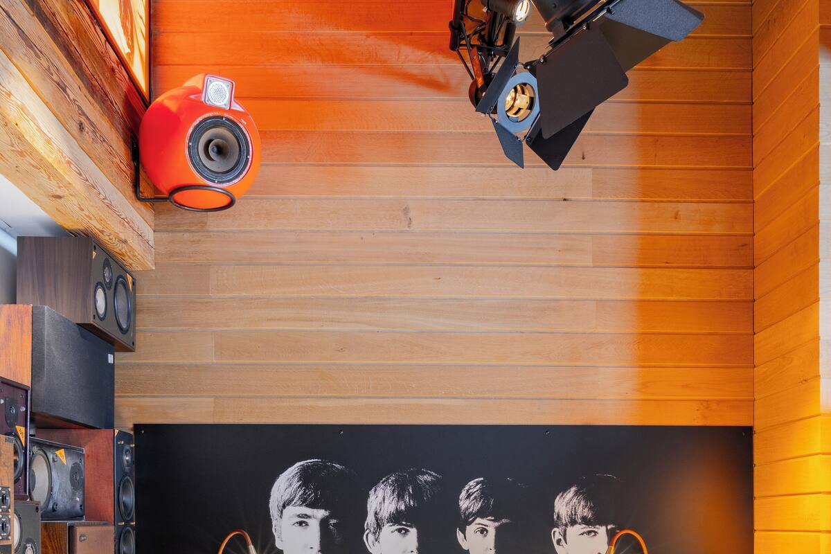 A wooden room with a bed, a guitar, and a wall-mounted speaker system.