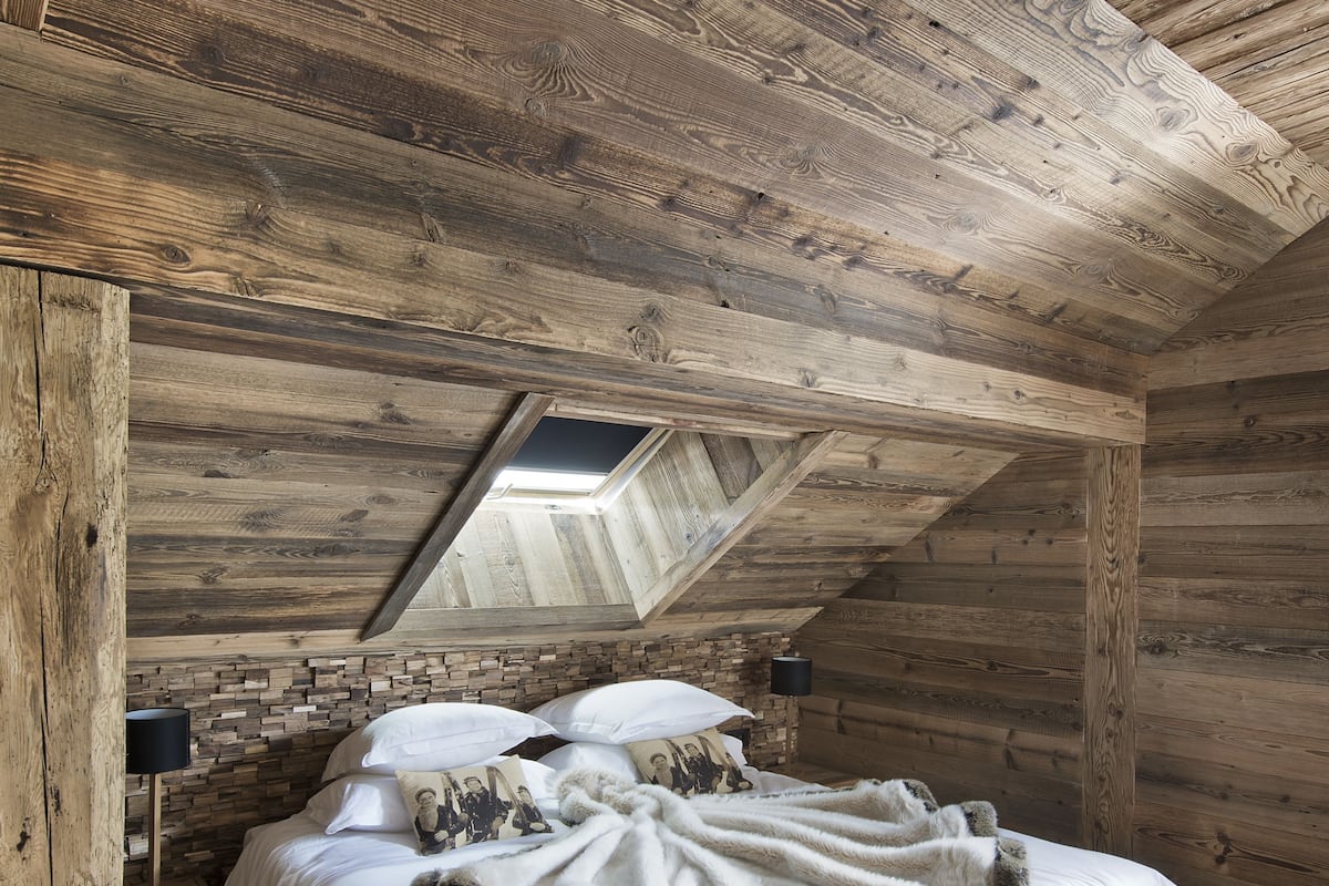 A wooden bedroom with a sloped ceiling, a skylight, a bed with white bedding, and two bedside tables.