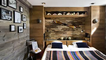 A modern hotel room with a wooden wall, a bed with a colorful striped blanket, a small desk with a globe and a toy airplane, and a shelf with model cars.