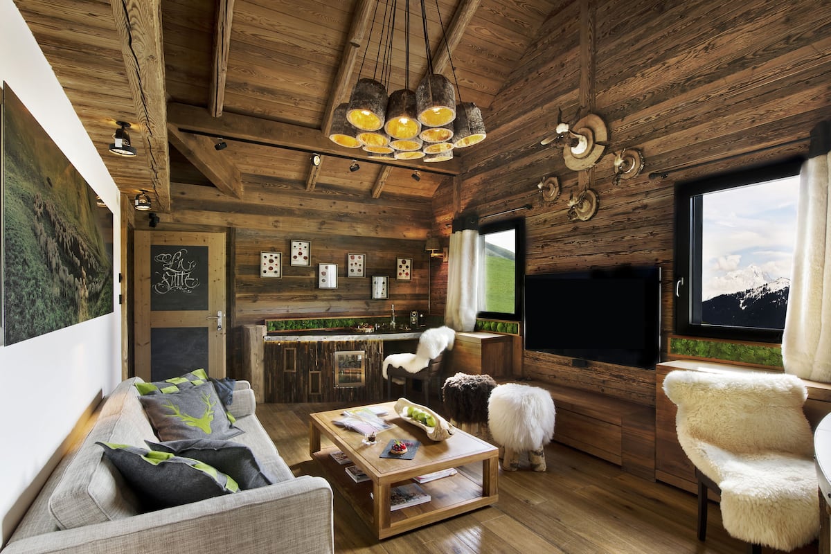 A rustic cabin interior with a wooden ceiling, a dining area, a kitchen, and a large window with a mountain view.