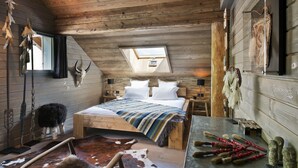 A rustic bedroom with a sloped ceiling, a skylight, a bed with a striped blanket, wooden nightstands, and a cowhide rug. - Les Rhodos (La Clusaz)