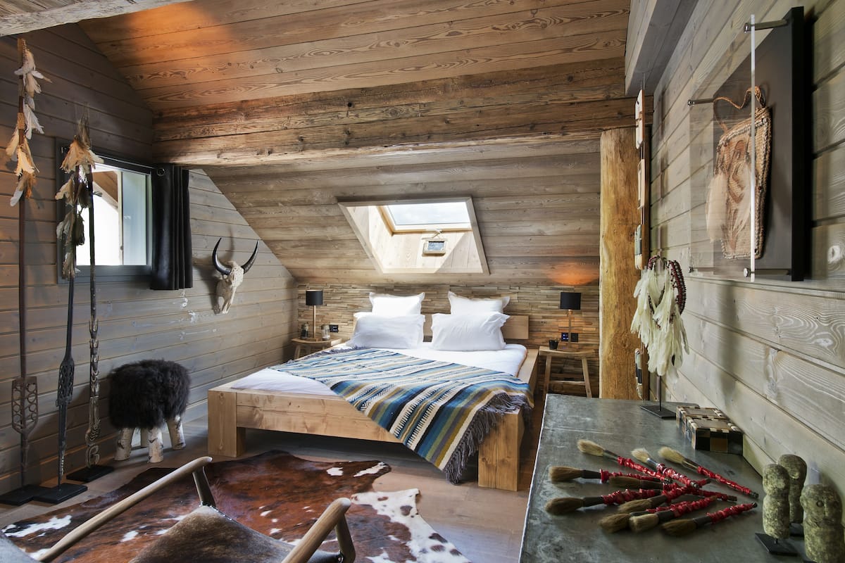 A rustic bedroom with a sloped ceiling, a skylight, a bed with a striped blanket, wooden nightstands, and a cowhide rug.