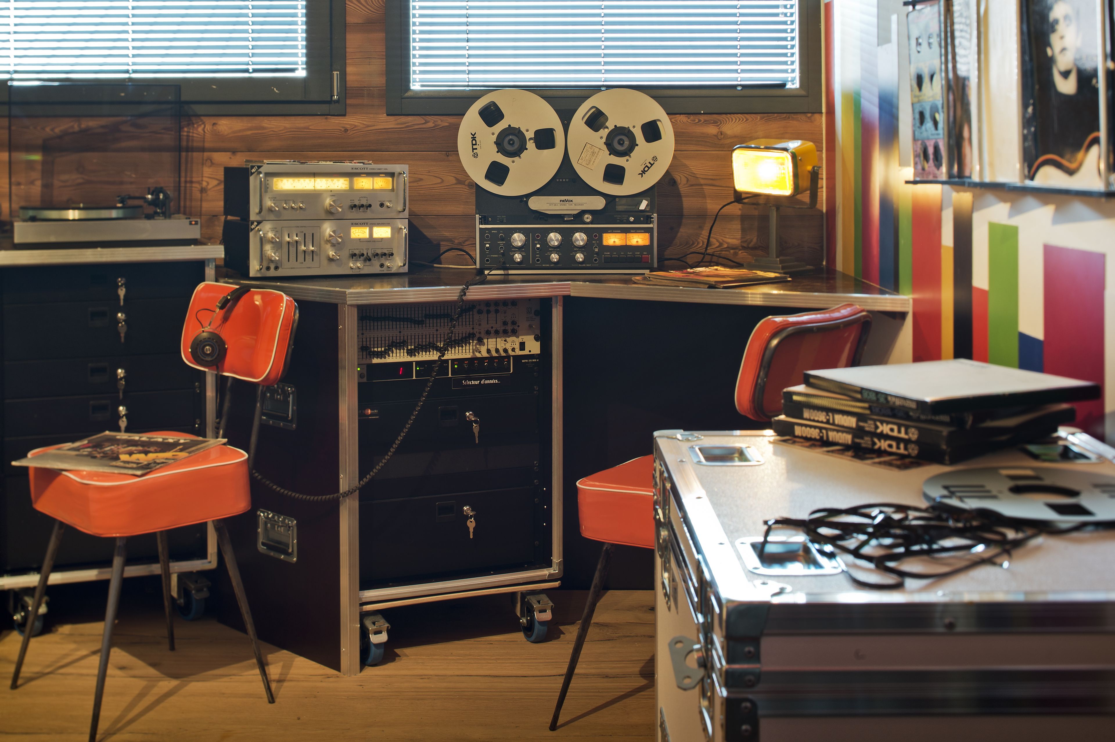 A recording studio with vintage equipment, including reel-to-reel tape recorders, mixing consoles, and a desk with chairs.