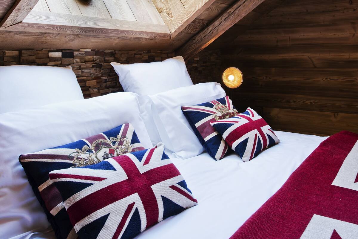 A bedroom with a sloped ceiling, a skylight, a bed with white bedding, and pillows with a Union Jack design.