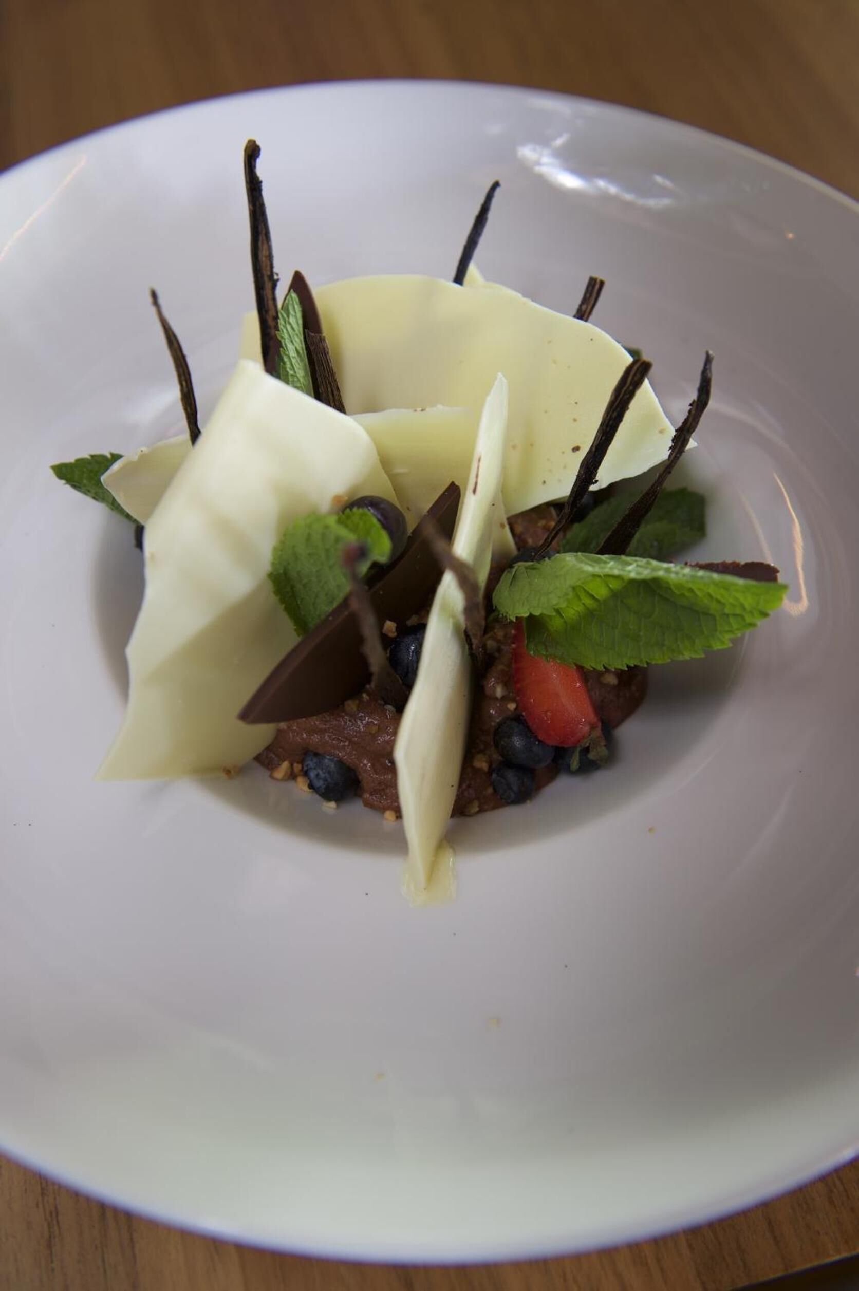 A dessert on a white plate with vanilla, chocolate, strawberries, and mint leaves.