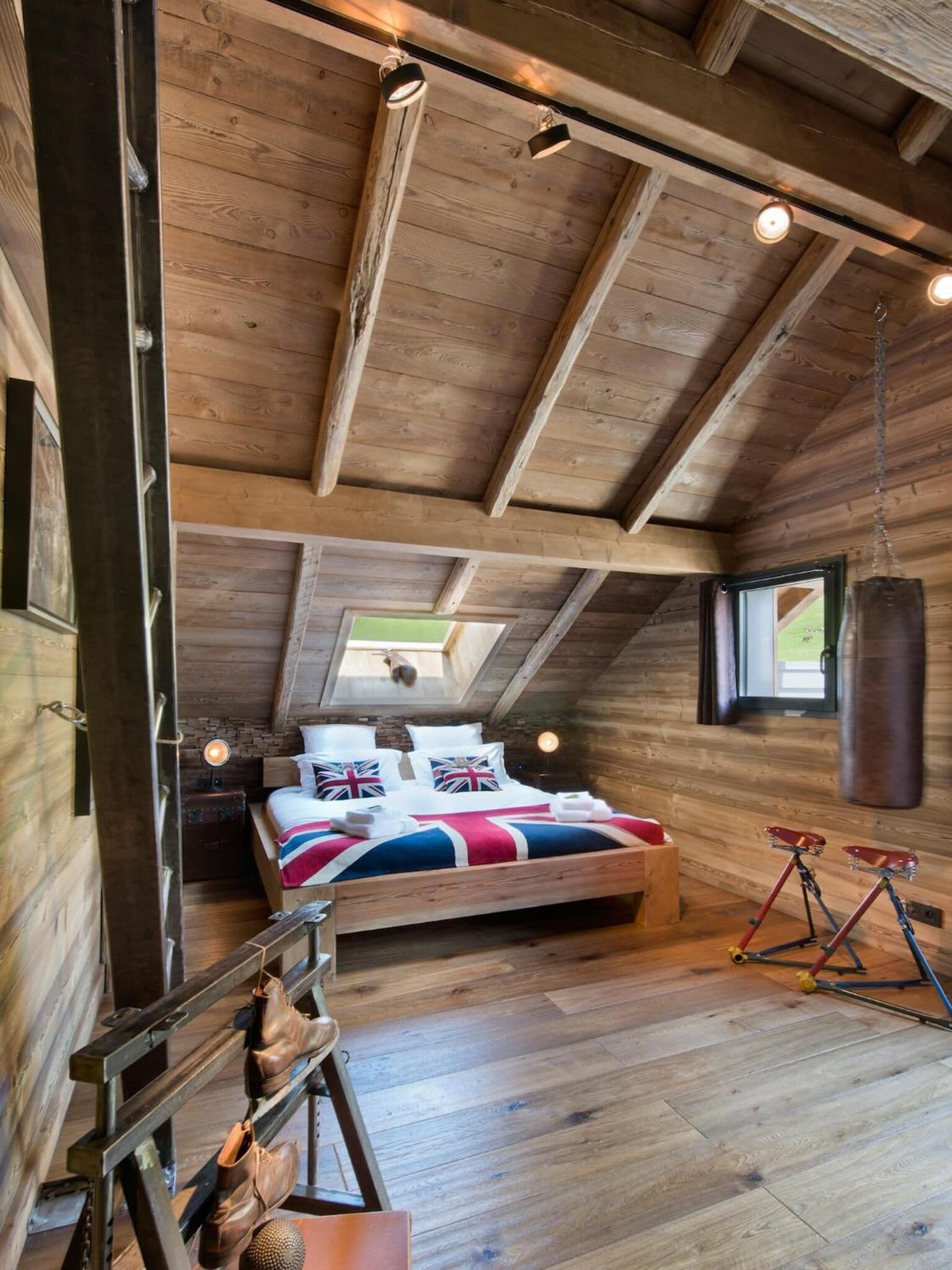 Une chambre mansardée chaleureuse avec un plafond en bois, un lit recouvert d’une couette ornée du drapeau britannique (Union Jack) et un sac de frappe.