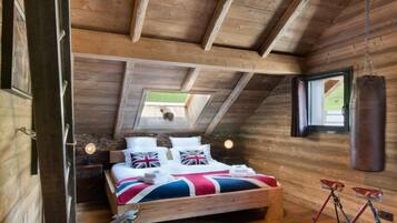 Une chambre mansardée chaleureuse avec un plafond en bois, un lit recouvert d’une couette ornée du drapeau britannique (Union Jack) et un sac de frappe.