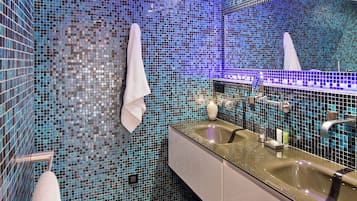 Un baño con paredes de mosaicos, un lavamanos y un espejo.