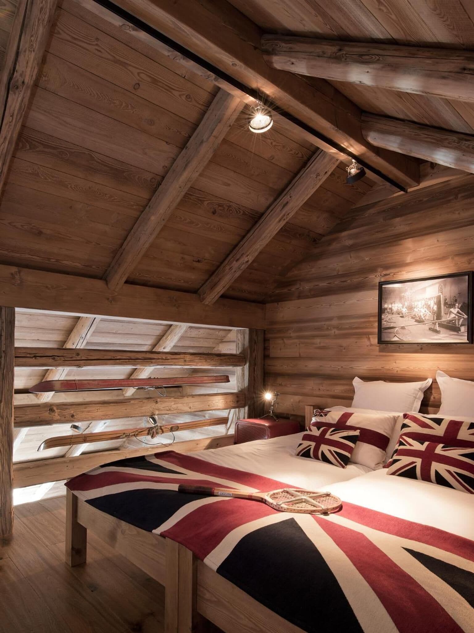 A wooden cabin bedroom with a bed, skis, and a framed picture on the wall.