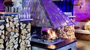 A rustic interior with a fireplace, wooden ceiling, and a stone wall. - Les Rhodos (La Clusaz)