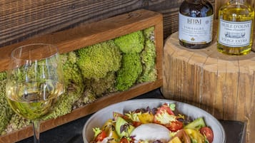 Une table en bois avec un verre de vin blanc, une bouteille de vinaigre EtBM et une bouteille d’huile d’olive.
