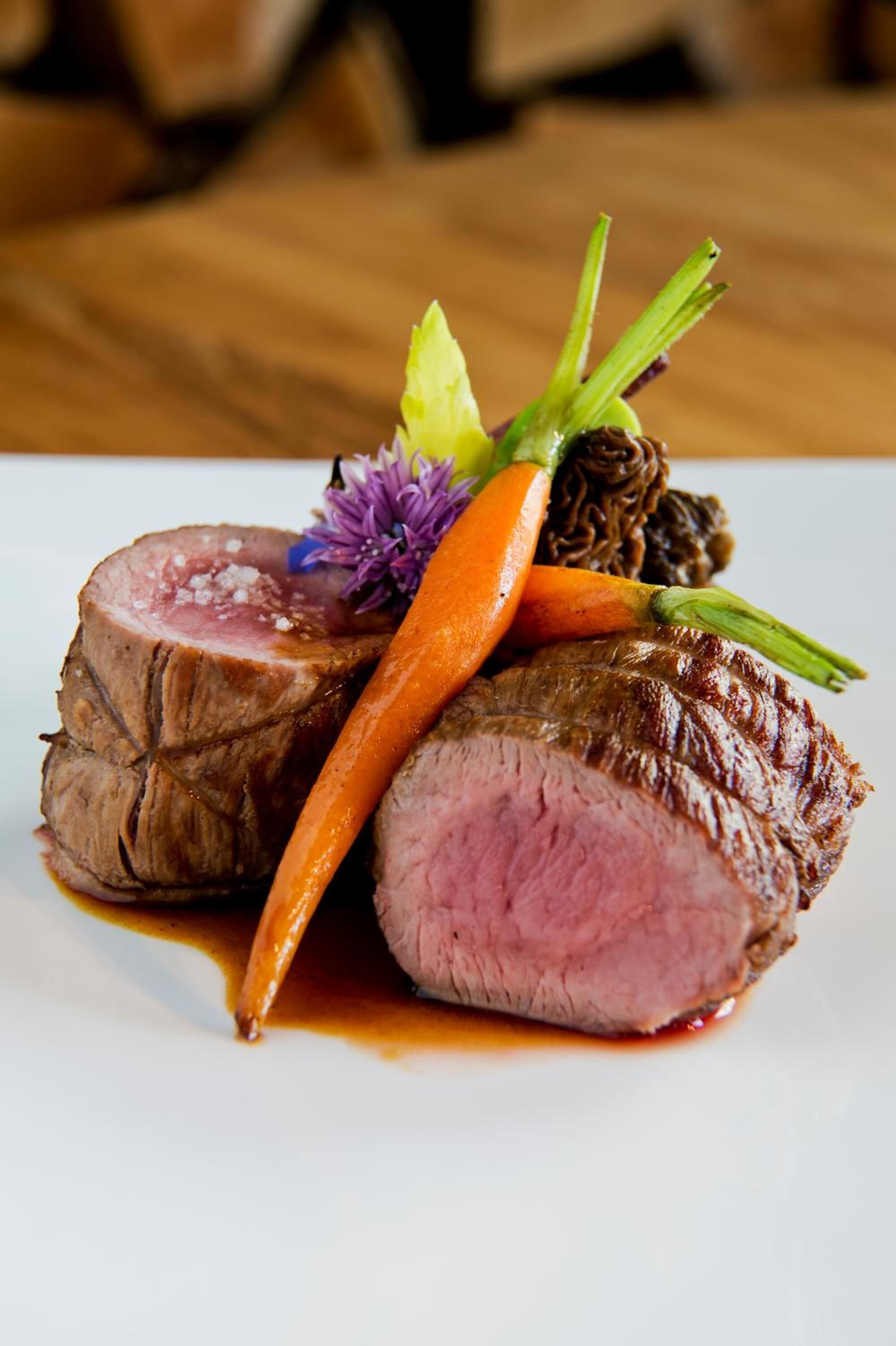 A plate of sliced beef with a garnish of carrot, purple flower, and green herbs.